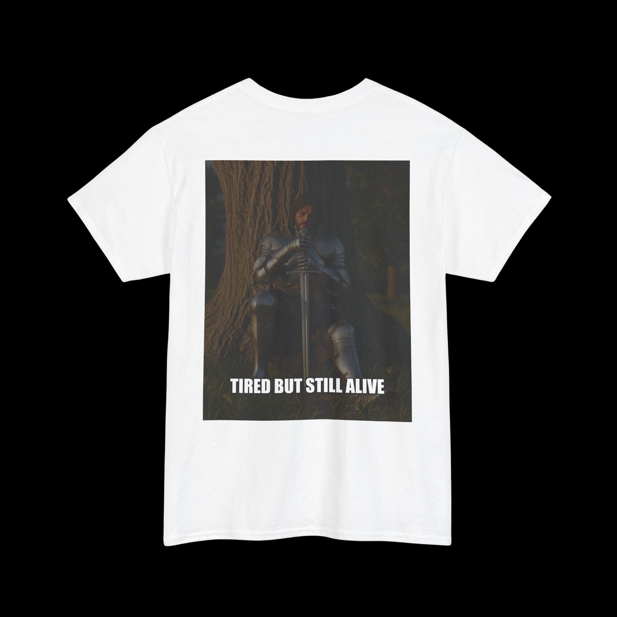 White t-shirt featuring a graphic of a tired but resolute knight in armor sitting with a sword, and the text "TIRED BUT STILL ALIVE". Ideal for expressing resilience and perseverance.